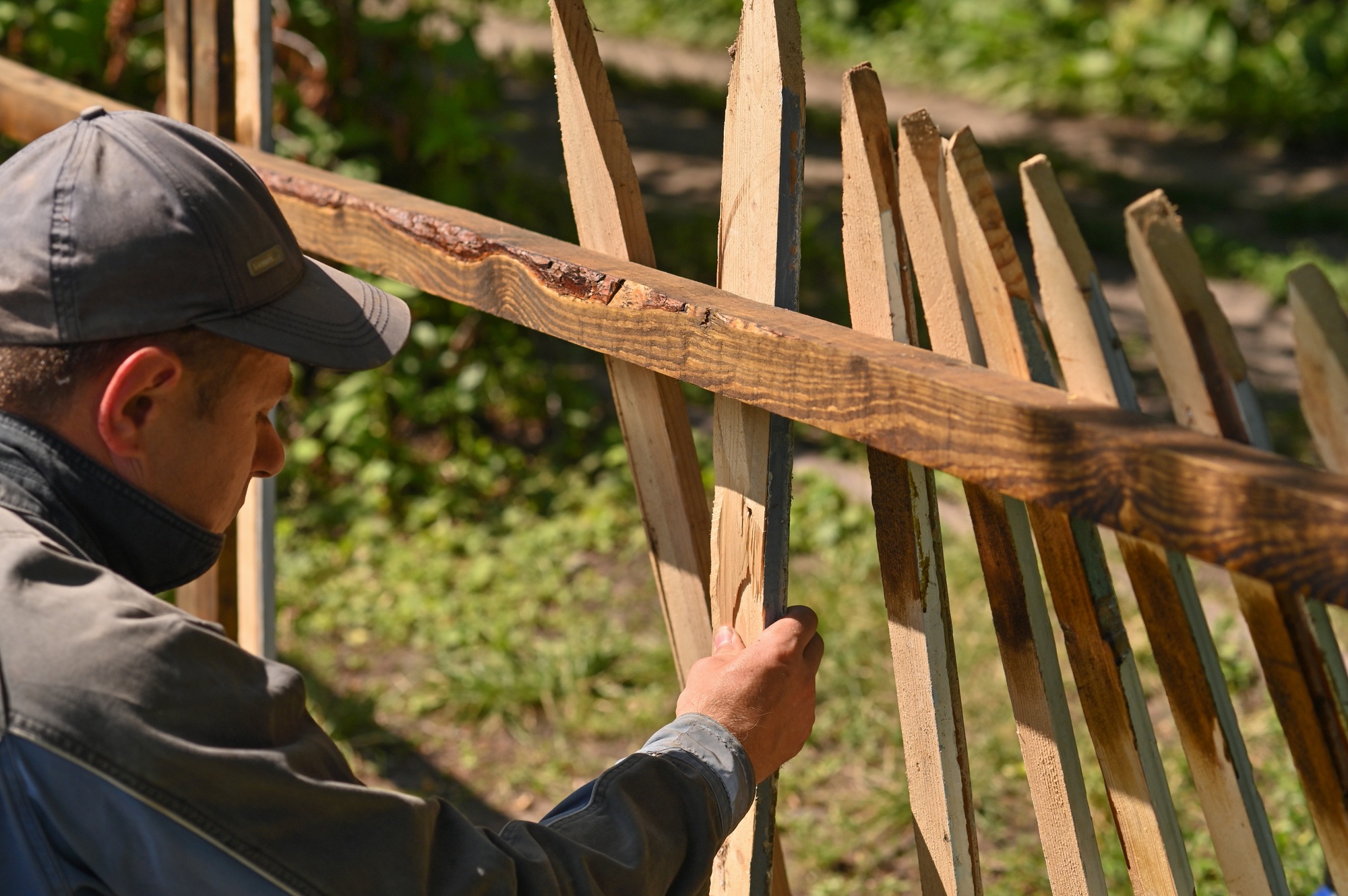 A male carpenter makes a fence outdoors